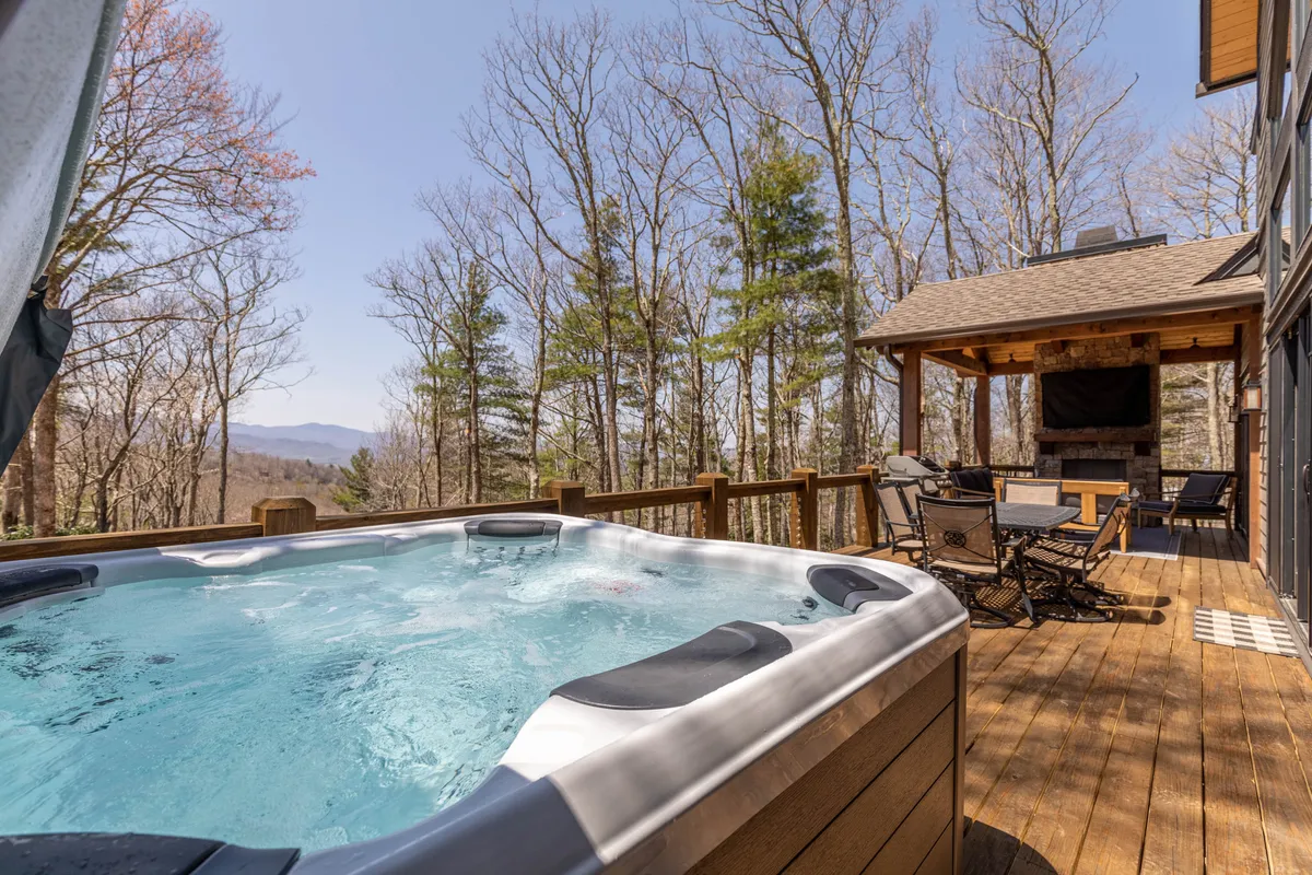 A serene deck scene featuring a bubbling hot tub, surrounded by tall trees and outdoor seating. The natural setting offers privacy and relaxation, perfect for unwinding after a day of exploration or enjoying a sunset soak with a loved one.