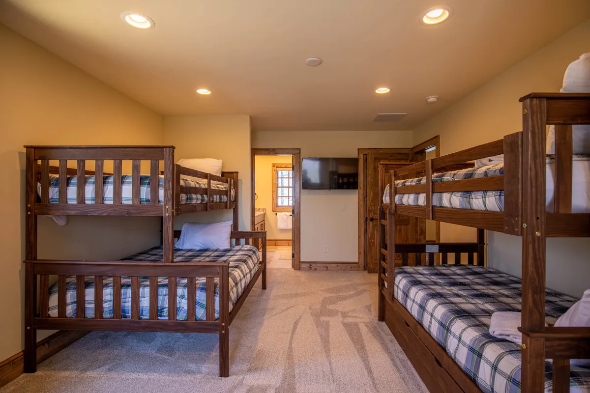 A family-friendly bunk suite featuring plaid bedding on two sets of bunk beds, a wall-mounted TV, and ample space for group gatherings. The playful and cozy ambiance encourages storytelling, games, and bonding moments.