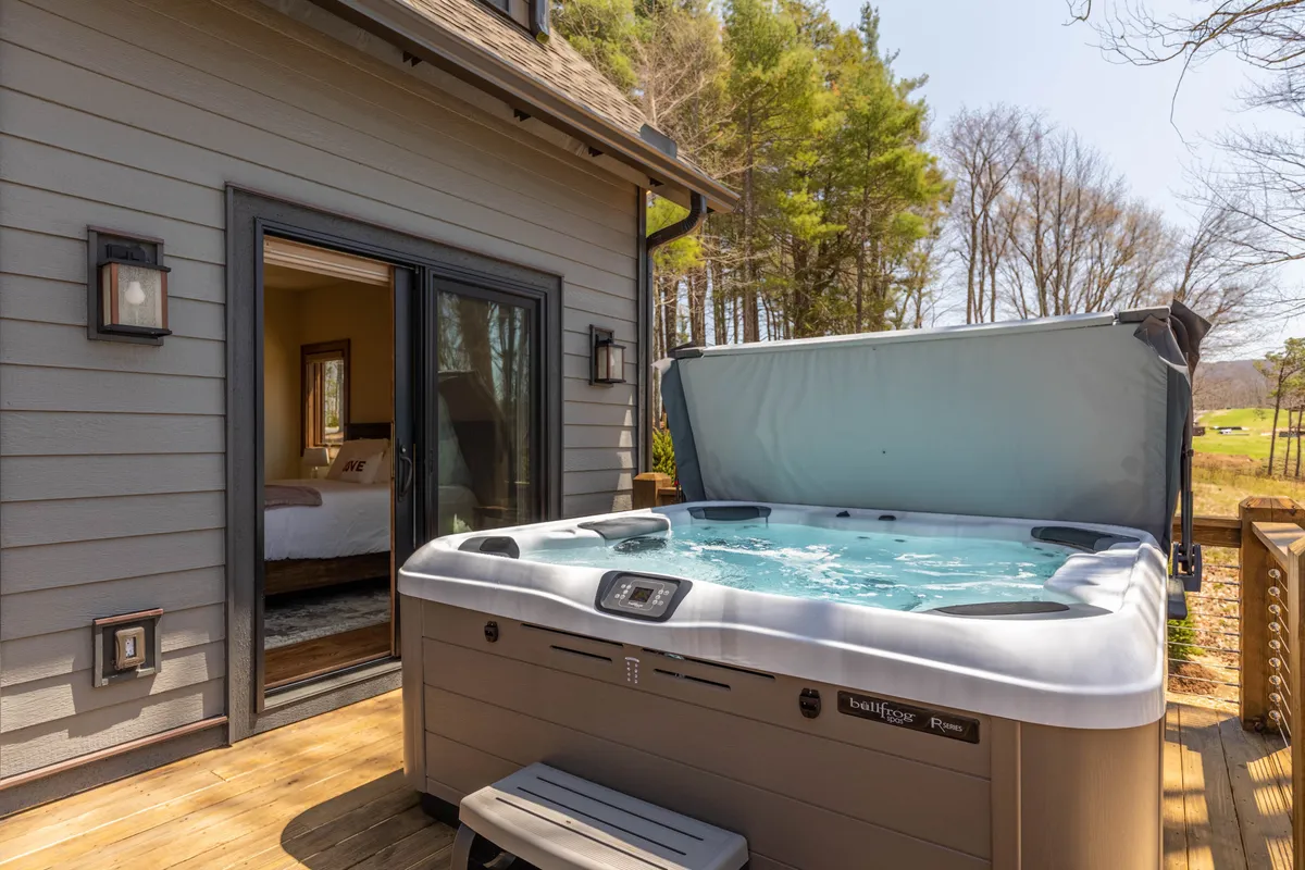 A tranquil hot tub set on a deck overlooks surrounding greenery, with a doorway leading to a cozy bedroom nearby. The setting is private and serene, ideal for relaxing after a day of adventure.