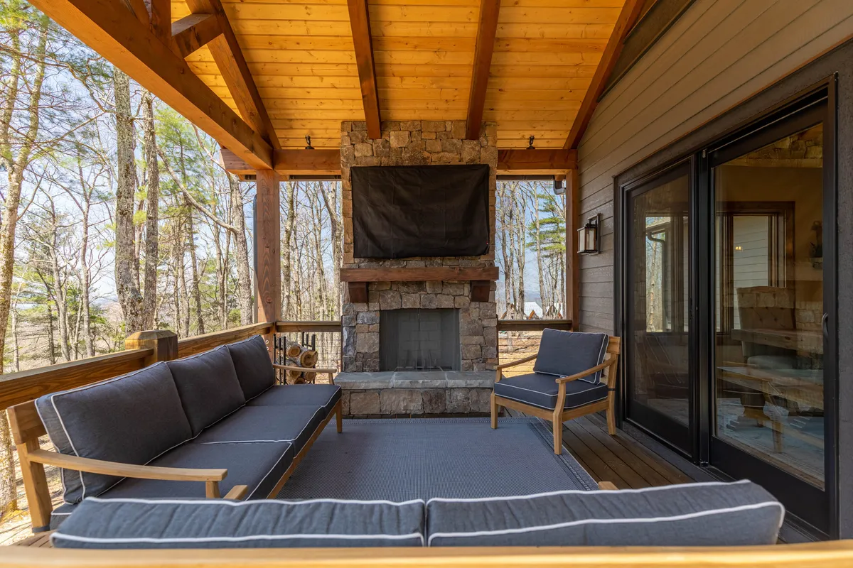 A cozy and inviting outdoor lounge area with a large stone fireplace, comfortable seating, and rustic wooden beams. The setting is perfect for relaxing evenings by the fire while taking in the surrounding nature.