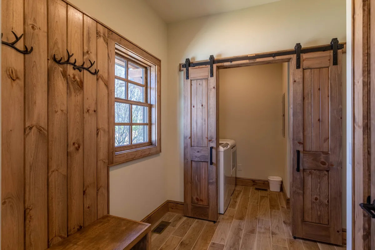 A functional mudroom with a wooden bench, sliding barn doors, and a window letting in natural light. The space is practical yet welcoming, ideal for storing boots and gear after outdoor adventures.