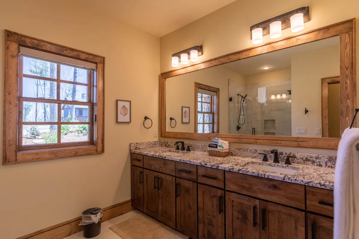 A serene bathroom space showcasing a double sink granite vanity with a large mirror, wooden window frame, and soft ambient lighting. The atmosphere is calm and inviting, suggesting a luxurious and upscale experience for morning or evening routines.