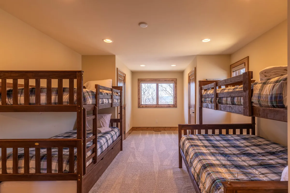 A cozy interior scene with a set of bunk beds, plaid bedding, and a window overlooking the outdoors. The inviting setup hints at sleepovers, storytelling, and children bonding in a communal, playful atmosphere.