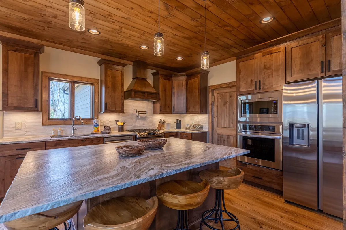 A cozy kitchen scene focused on the island, with wood cabinetry, pendant lights, and more stainless steel appliances. The space feels welcoming and designed for both cooking and socializing.